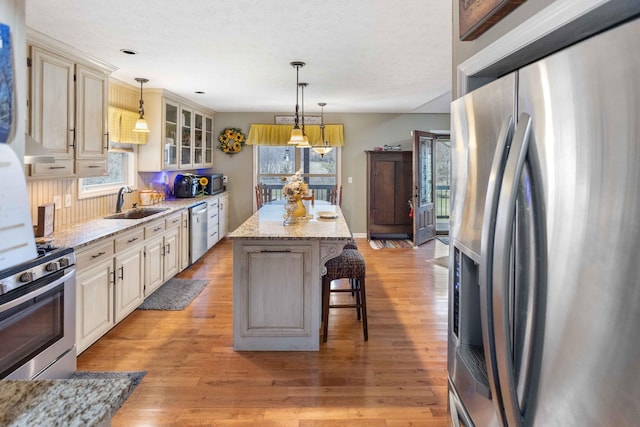 kitchen featuring a center island, a breakfast bar area, appliances with stainless steel finishes, light wood-style floors, and glass insert cabinets