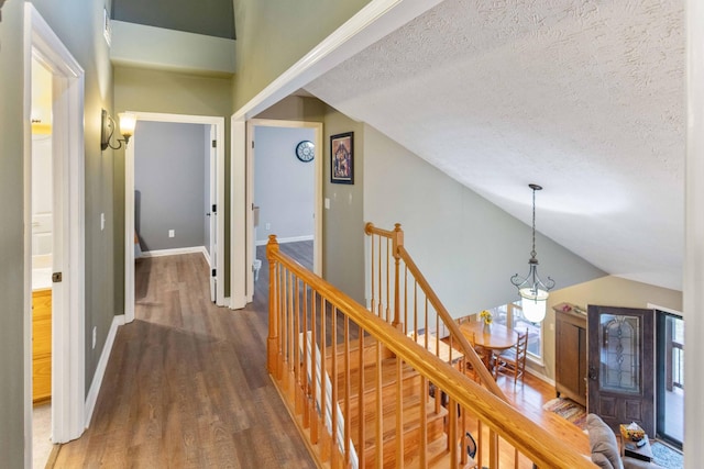 corridor featuring lofted ceiling, dark wood finished floors, a textured ceiling, and an upstairs landing