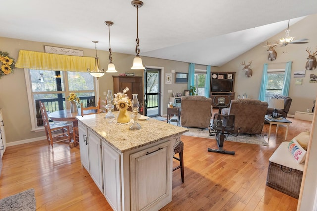 kitchen featuring a kitchen island, a kitchen breakfast bar, hanging light fixtures, vaulted ceiling, and light wood-type flooring