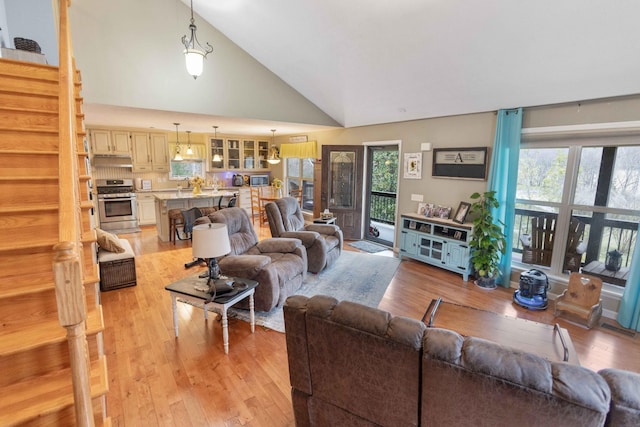 living room with light wood-type flooring, high vaulted ceiling, stairway, and a wealth of natural light