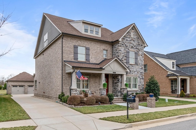 view of front of house featuring covered porch, brick siding, a detached garage, stone siding, and a front lawn