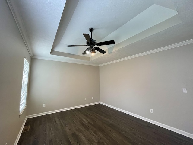 empty room with dark wood-style floors, a tray ceiling, visible vents, and baseboards