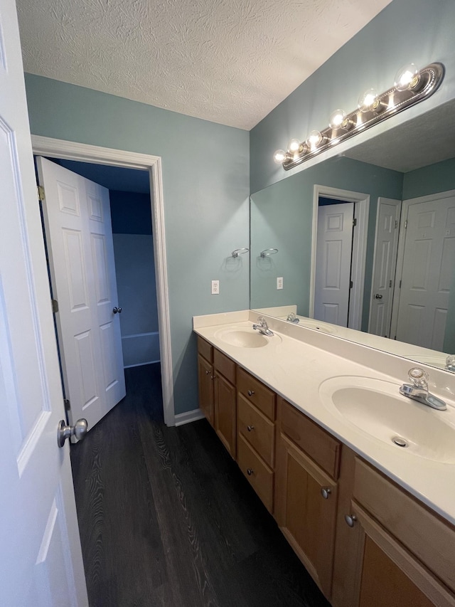 bathroom with a textured ceiling, double vanity, wood finished floors, and a sink