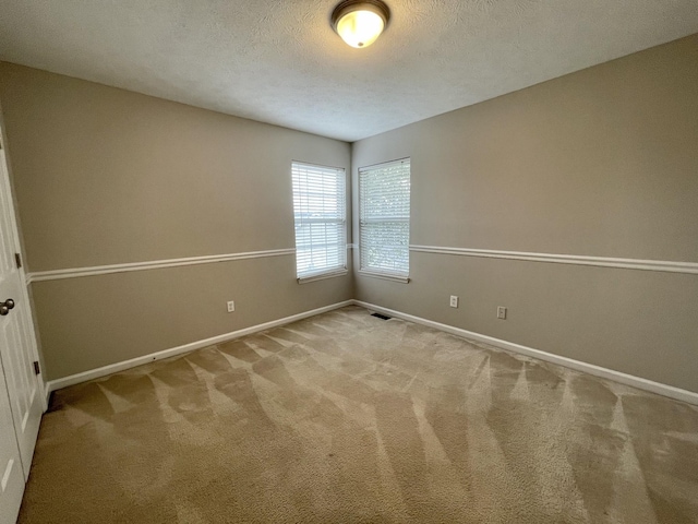 carpeted empty room with visible vents, a textured ceiling, and baseboards