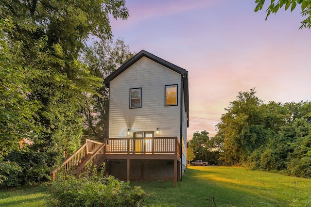 back of house at dusk with a deck, a yard, and stairway