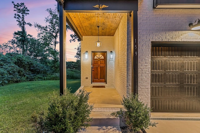 exterior entry at dusk with a garage, brick siding, and a lawn