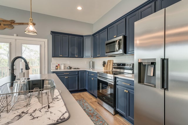 kitchen with blue cabinets, light countertops, appliances with stainless steel finishes, light wood-type flooring, and backsplash