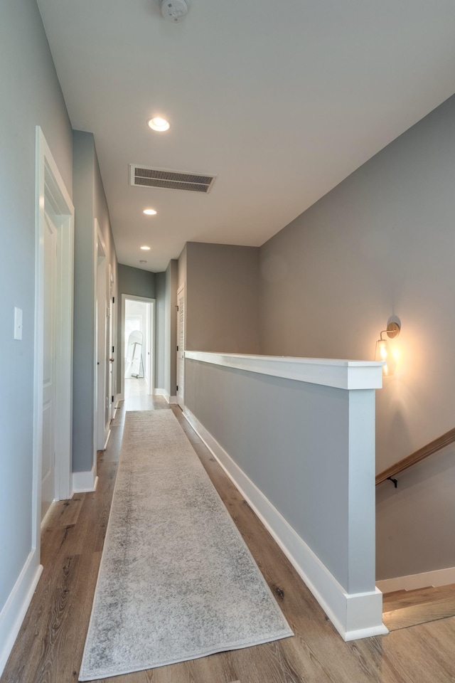 hall with visible vents, wood finished floors, an upstairs landing, and baseboards