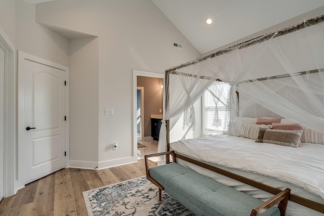 bedroom with high vaulted ceiling, visible vents, baseboards, and wood finished floors