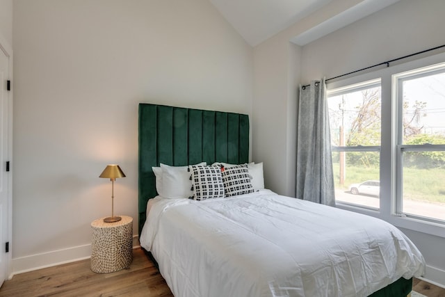 bedroom with lofted ceiling, multiple windows, baseboards, and wood finished floors