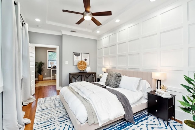 bedroom featuring a tray ceiling, recessed lighting, visible vents, a decorative wall, and light wood-style floors