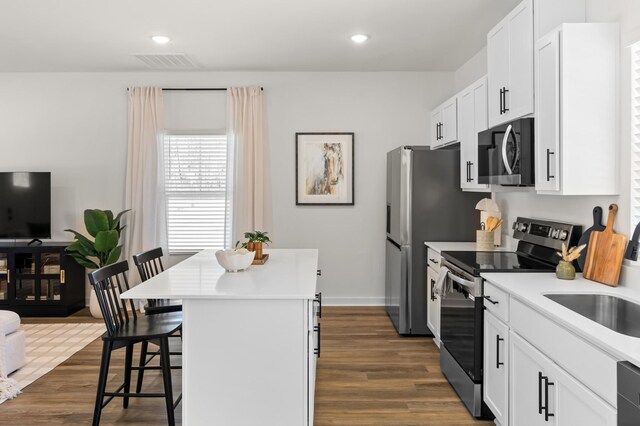 kitchen featuring dark wood-type flooring, a breakfast bar, a kitchen island, visible vents, and appliances with stainless steel finishes