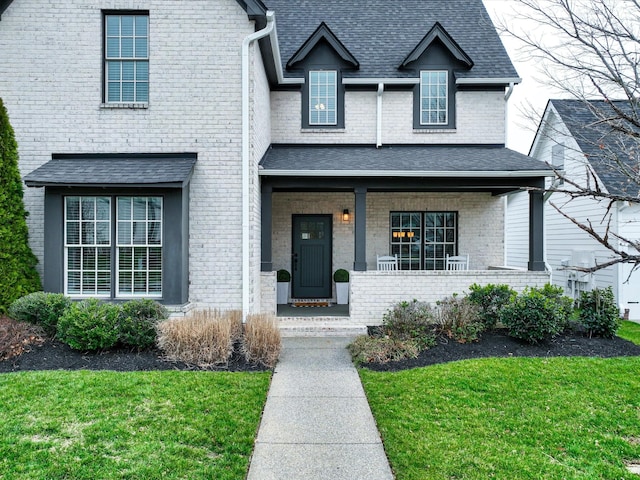 traditional home with a porch, brick siding, a shingled roof, and a front lawn