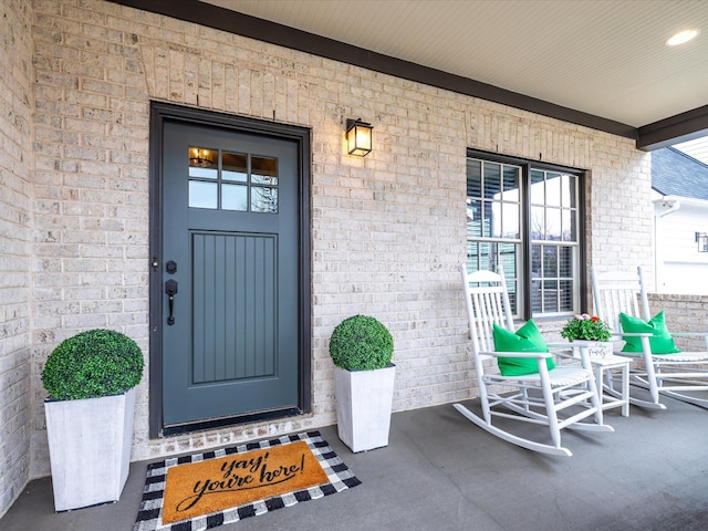 property entrance with a porch and brick siding