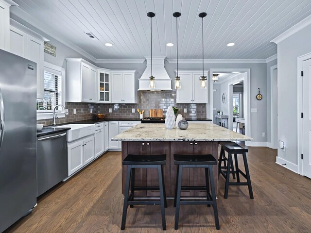 kitchen with tasteful backsplash, white cabinets, custom range hood, appliances with stainless steel finishes, and a sink