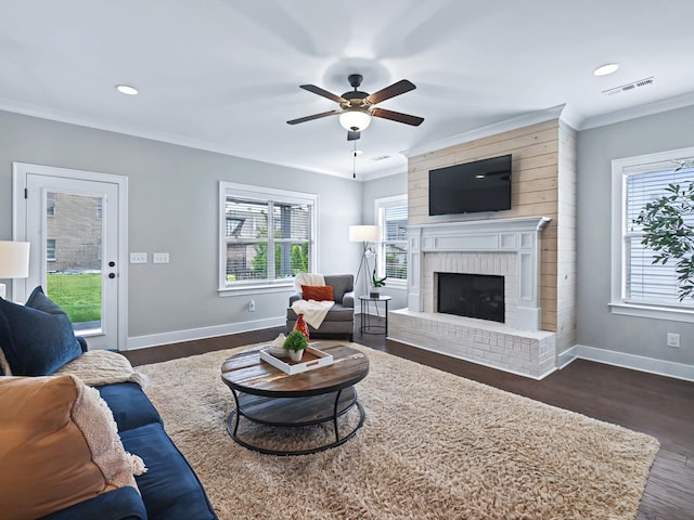 living room with dark wood-type flooring, a fireplace, visible vents, baseboards, and ornamental molding