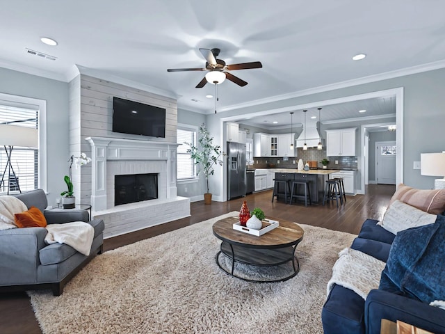 living area with ornamental molding, dark wood-style flooring, a fireplace, and visible vents