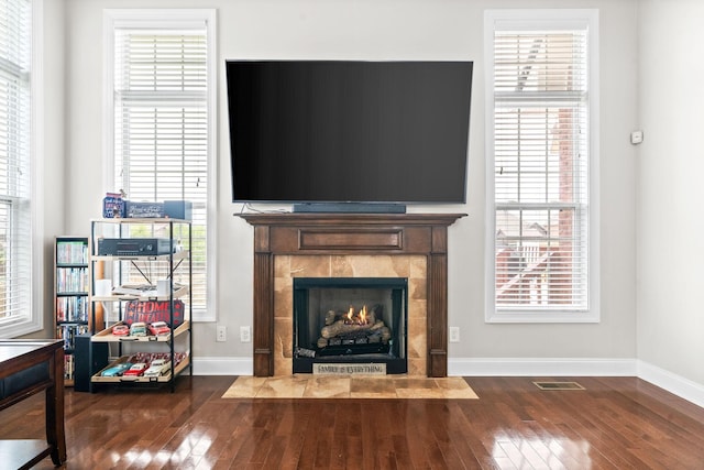 unfurnished living room featuring a healthy amount of sunlight, wood-type flooring, baseboards, and a tile fireplace