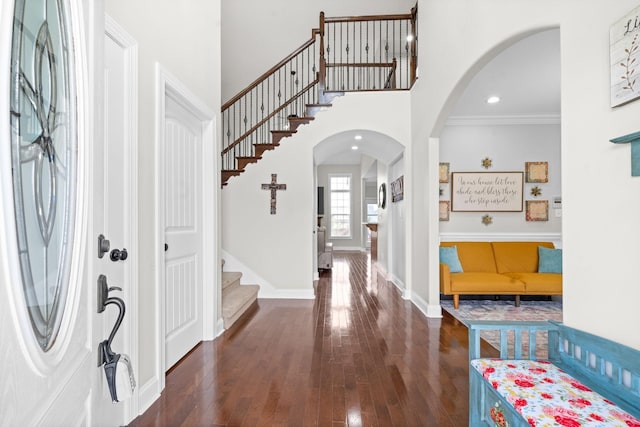 foyer entrance with baseboards, arched walkways, a towering ceiling, hardwood / wood-style flooring, and stairs