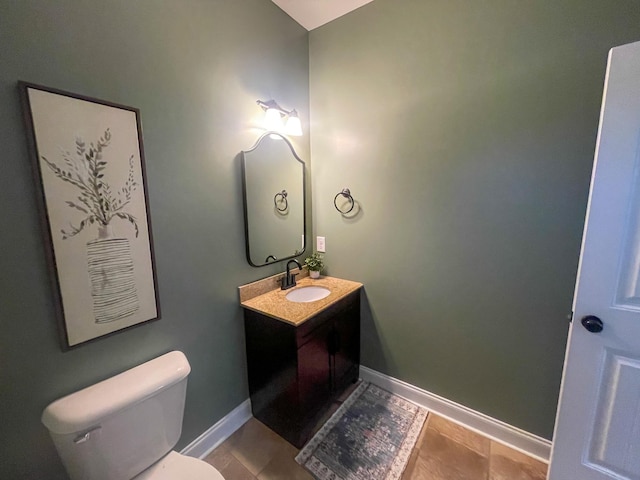 half bath with toilet, baseboards, and vanity