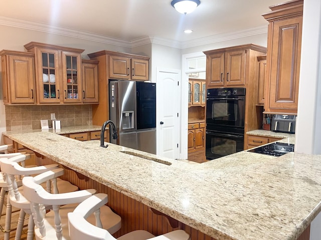 kitchen with brown cabinets, a breakfast bar area, decorative backsplash, glass insert cabinets, and black appliances