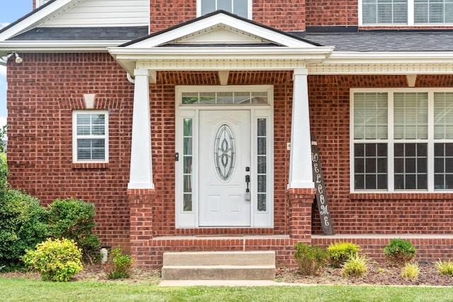 entrance to property with a shingled roof and brick siding