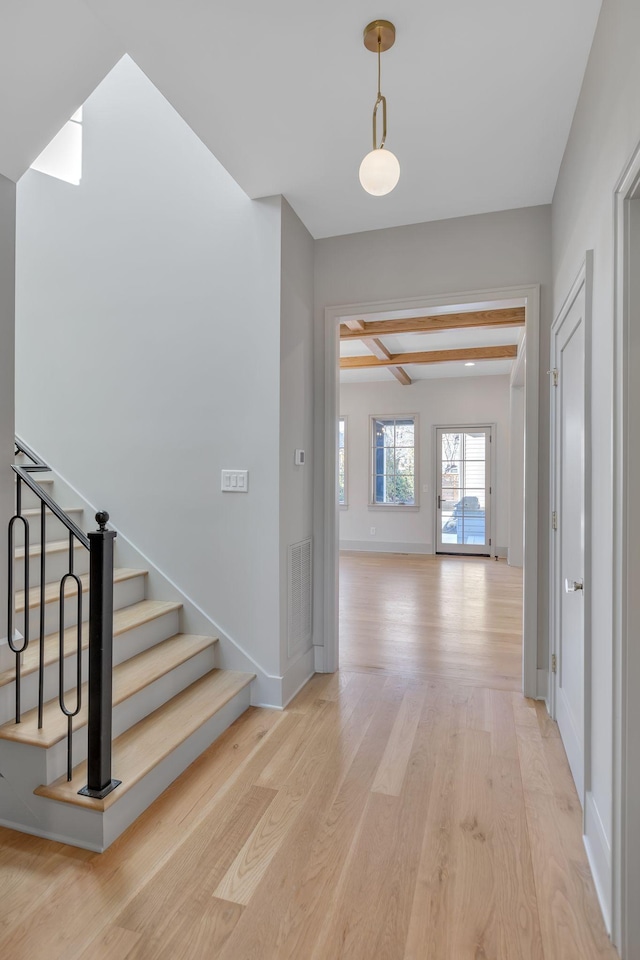 interior space with visible vents, stairway, light wood-style floors, beamed ceiling, and baseboards