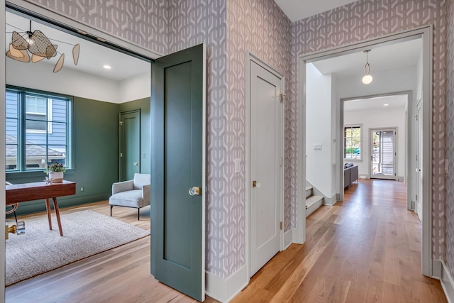 corridor featuring baseboards, stairway, light wood-style flooring, and wallpapered walls