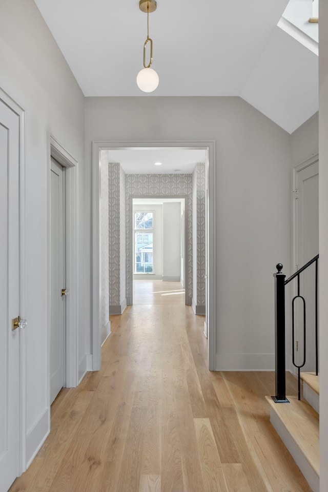 hall with baseboards, vaulted ceiling, light wood finished floors, and wallpapered walls