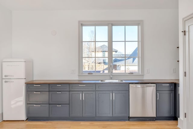 kitchen featuring light wood finished floors, gray cabinets, stainless steel dishwasher, freestanding refrigerator, and a sink