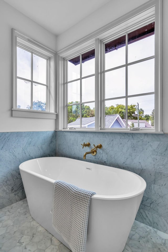 full bathroom featuring marble finish floor, a soaking tub, a wealth of natural light, and tile walls