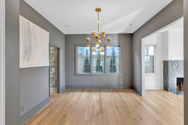 unfurnished dining area with light wood finished floors, a premium fireplace, baseboards, and a chandelier