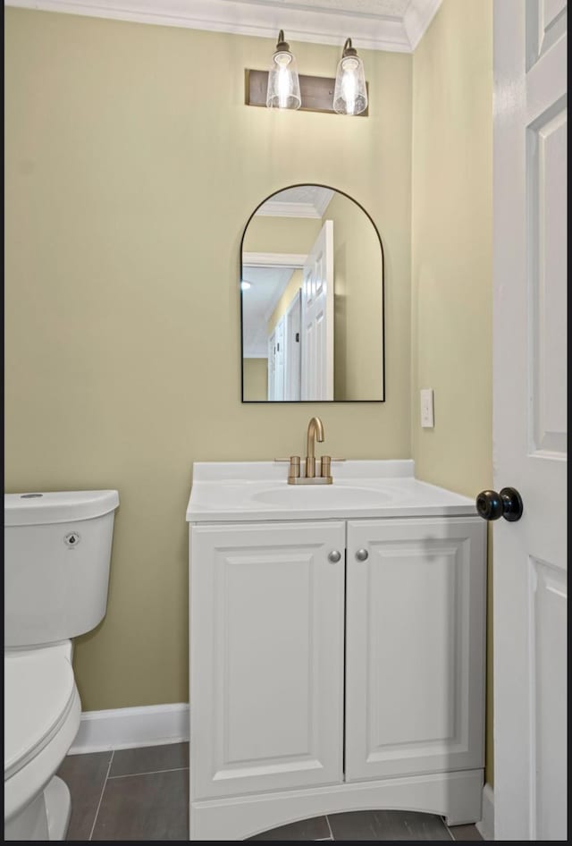 bathroom with toilet, ornamental molding, vanity, baseboards, and tile patterned floors