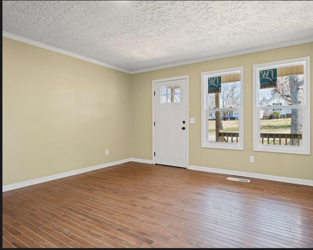 foyer entrance with ornamental molding, wood-type flooring, visible vents, and baseboards