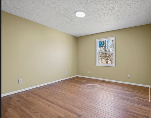 unfurnished room featuring hardwood / wood-style flooring, baseboards, and a textured ceiling