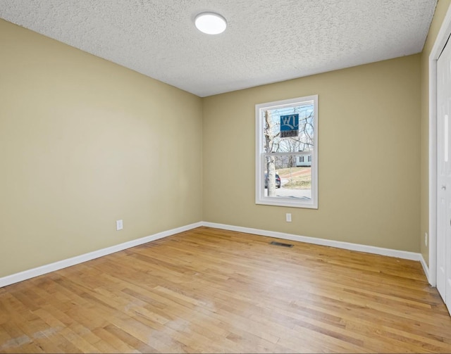 empty room featuring a textured ceiling, light wood-type flooring, visible vents, and baseboards