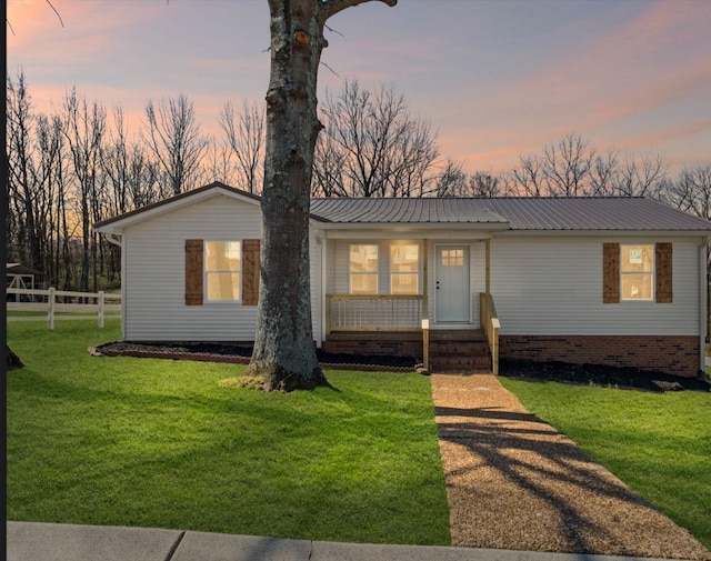 view of front of house with covered porch, metal roof, a lawn, and fence