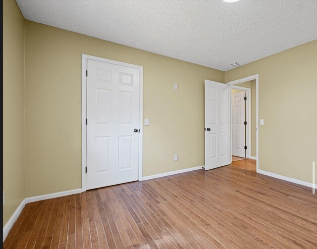 unfurnished bedroom with a textured ceiling, baseboards, and wood finished floors