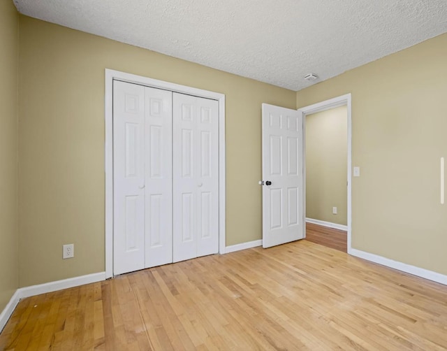 unfurnished bedroom with baseboards, a closet, a textured ceiling, and light wood-style floors