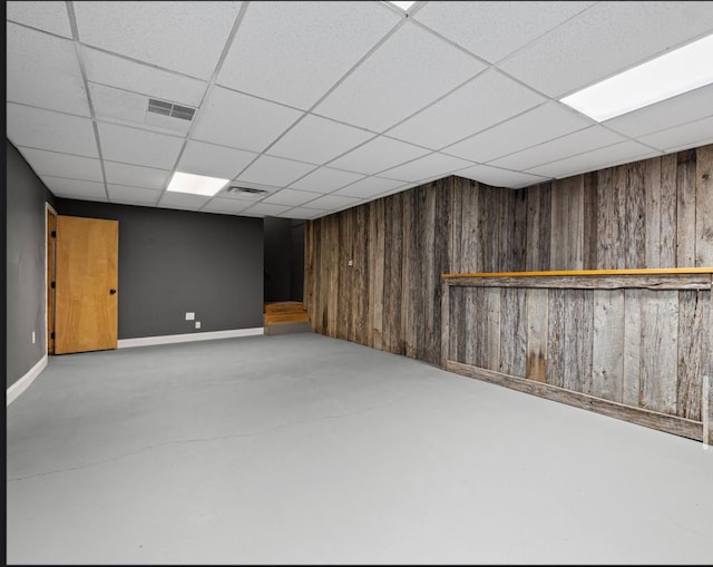 finished basement with a paneled ceiling, visible vents, and wood walls