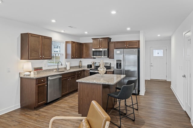 kitchen featuring dark wood finished floors, appliances with stainless steel finishes, a kitchen breakfast bar, a sink, and recessed lighting