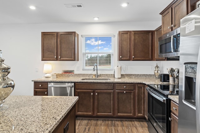 kitchen featuring visible vents, dark wood finished floors, light stone counters, appliances with stainless steel finishes, and a sink