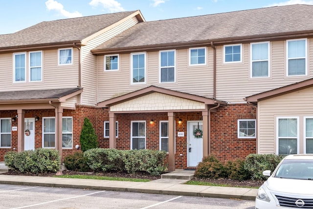 townhome / multi-family property featuring brick siding, uncovered parking, and roof with shingles