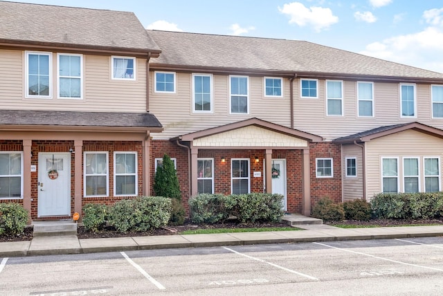 townhome / multi-family property featuring brick siding, roof with shingles, and uncovered parking