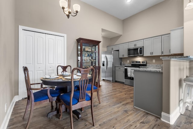 dining room with a towering ceiling, light wood-style floors, baseboards, and a notable chandelier