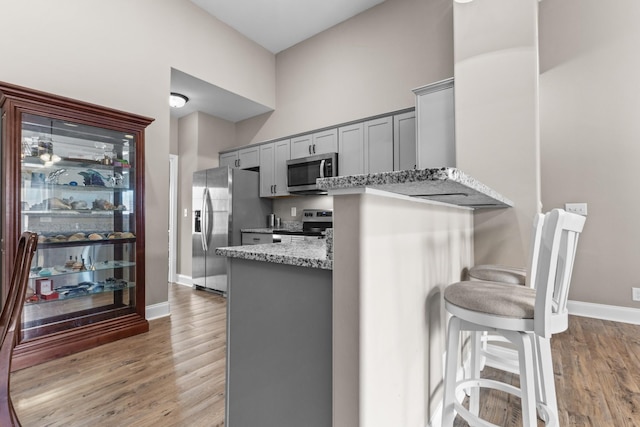 kitchen with light wood finished floors, stainless steel appliances, gray cabinets, light stone countertops, and baseboards