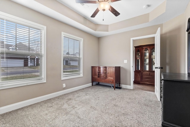 sitting room with a raised ceiling, light carpet, ceiling fan, and baseboards