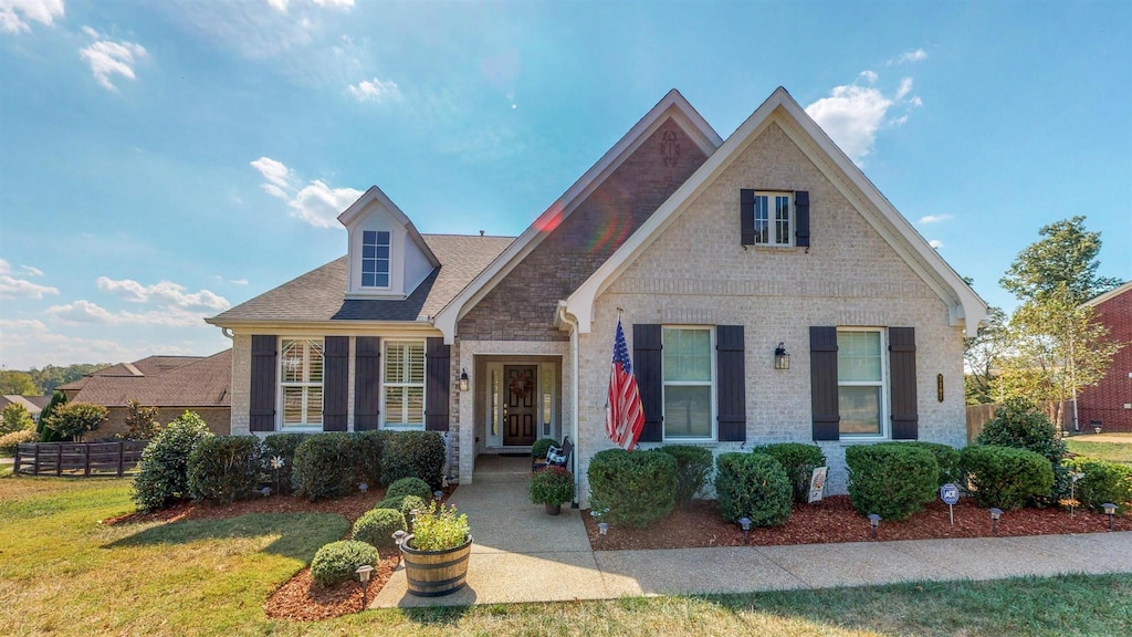 view of front of home with brick siding, a shingled roof, fence, and a front yard