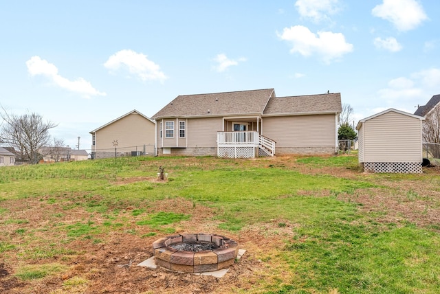 back of property with fence, a fire pit, and a yard