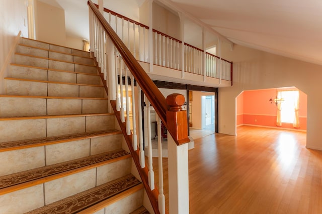 stairway with baseboards, high vaulted ceiling, arched walkways, and wood finished floors